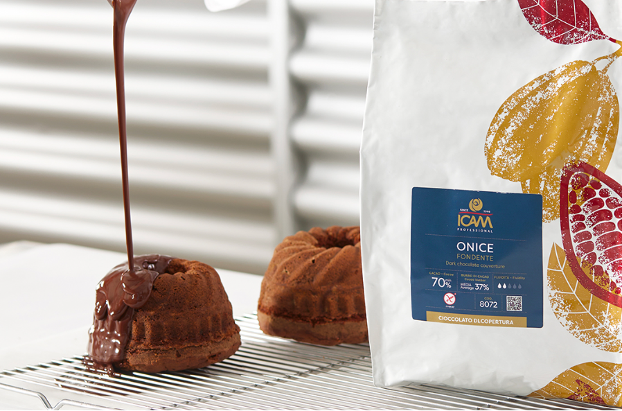 Person pouring chocolate sauce onto a dessert with a bag of ICAM chocolate powder in the foreground.